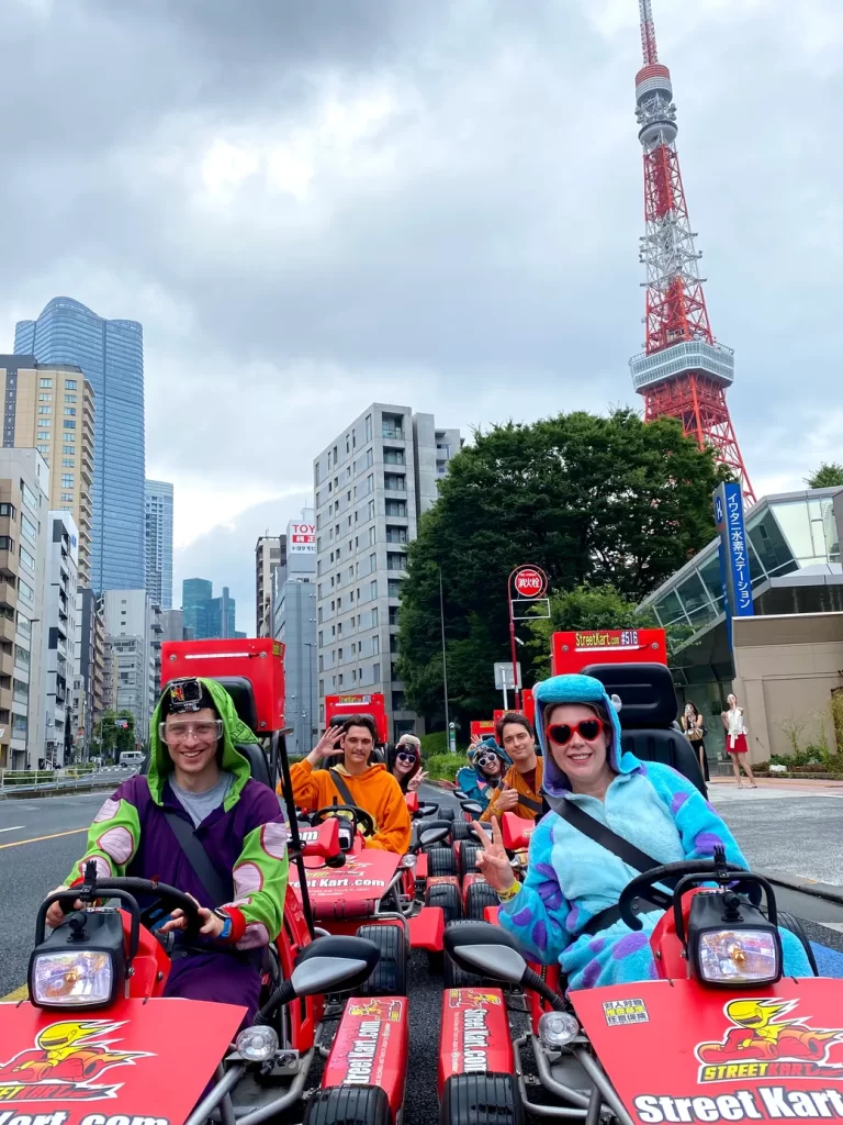 IMG_4691 - StreetKart Group of people in colorful onesies riding red Street Kart go-karts down a city street with Tokyo Tower in the background.